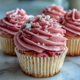 Moist, blush-pink Pink Velvet Cupcakes with Vanilla Buttercream Frosting sit on a cooling rack.