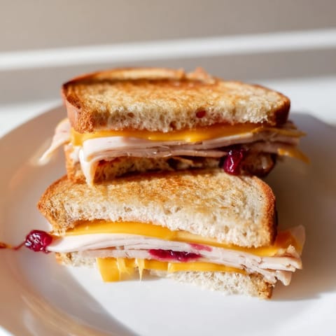 Smoked turkey grilled cheese sandwich, sliced diagonally on a rustic wooden board beside a small salad.  