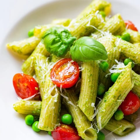 Fresh Green Pesto Pasta Salad served on a white plate with grated Parmesan and basil leaves garnish.  