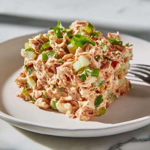 Freshly prepared Spicy Zesty Tuna Salad with a creamy red-speckled dressing, garnished with parsley and served alongside whole-grain bread.
