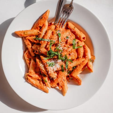 Spoonful of Creamy Roasted Red Pepper Pasta reveals smooth sauce clinging to penne, with steam rising over a rustic wooden table.