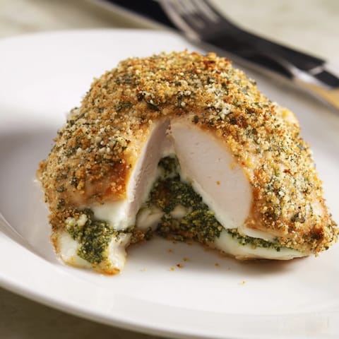 Four servings of Mozzarella & Pesto Stuffed Chicken plated beside a vibrant green salad and roasted red peppers for a complete Italian meal.  