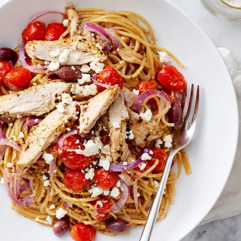 Juicy sliced chicken crowns a steaming bowl of Greek Chicken Spaghetti speckled with red onion and parsley.