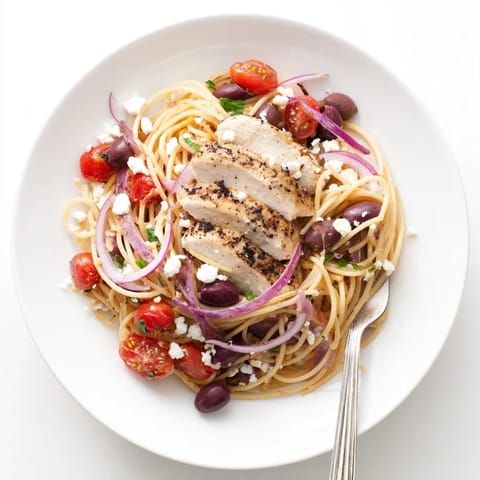 Tender grilled Greek Chicken Spaghetti twirled with cherry tomatoes, olives, and crumbled feta over a vibrant skillet.
