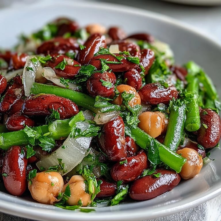 Fresh Three-Bean Salad displayed on a rustic wooden table, with a tangy apple cider vinaigrette glistening on the chickpeas and crisp celery slices.  