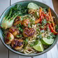 A close-up of an Asian Noodle Bowl with Shrimp and Scallops, garnished with fresh cilantro and lime wedges.